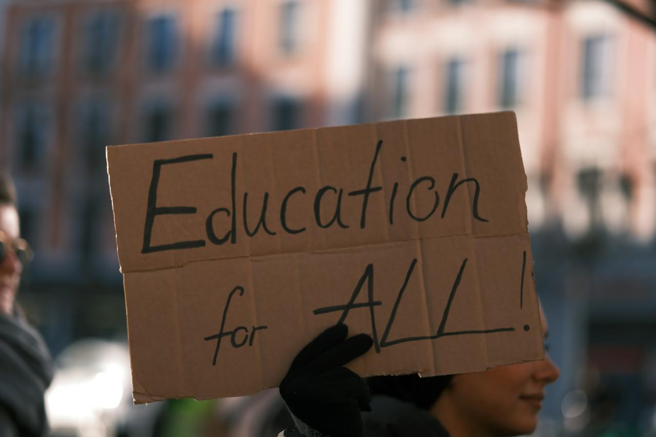 person holding up a sign that says education for all