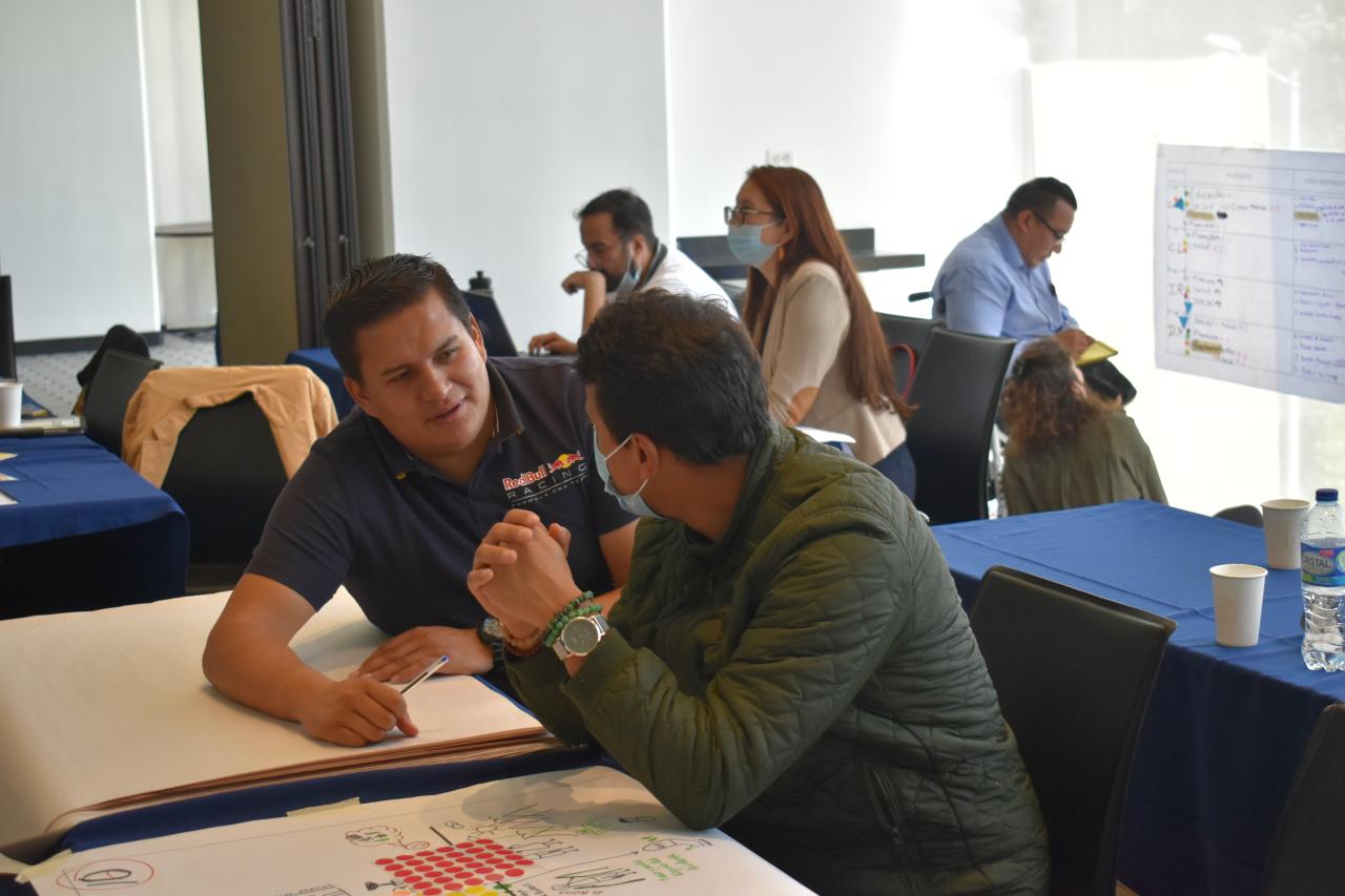 Two men sitting at a table talking during during Polus' Model Coherency human service program design workshop in Colombia