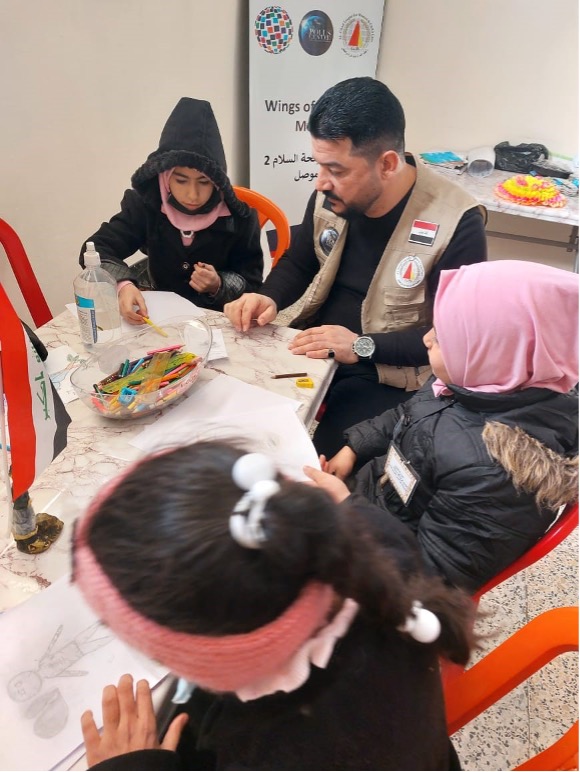 Staff member of Al-Ghad seated, overseeing three children who are drawing and painting