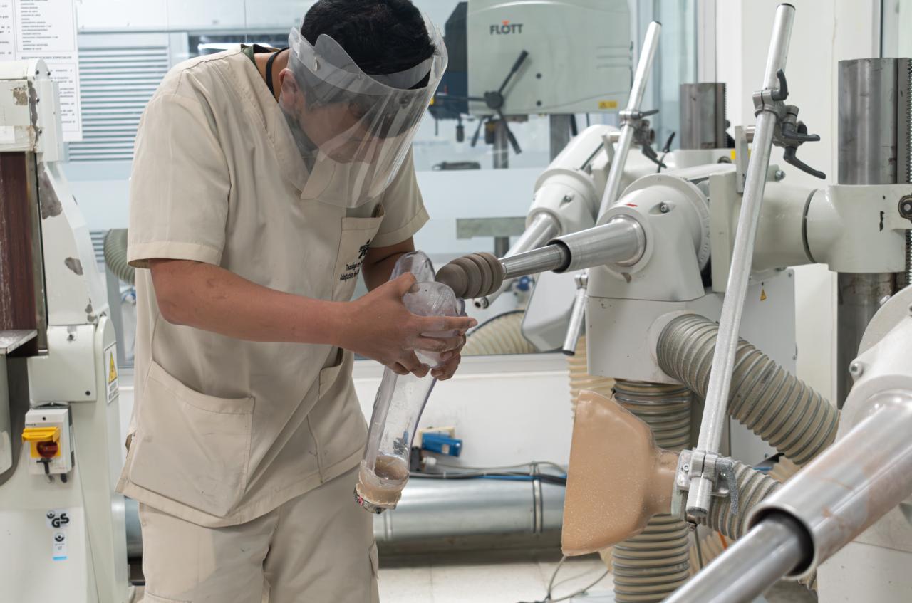 Prosthetic technician in Colombia wearing protective gear using a machine to build a new device.
