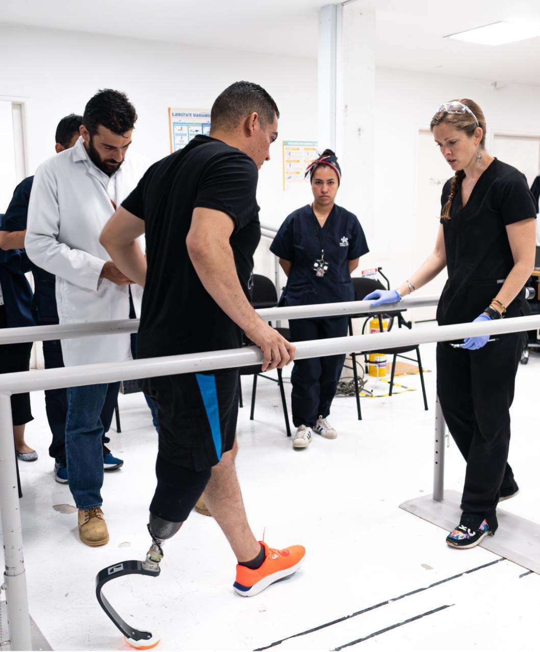 Man testing his new prosthetic leg with prosthetic technicians around him at clinic in Colombia. The new limb is a blade for running.