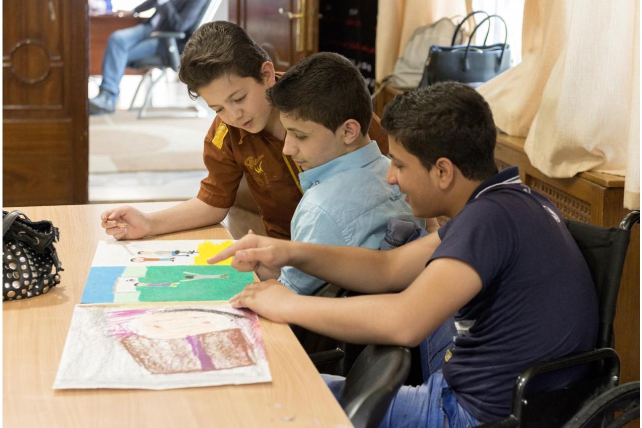 Three children sitting looking at drawings they've made at in the expressive arts program in Jordan. 