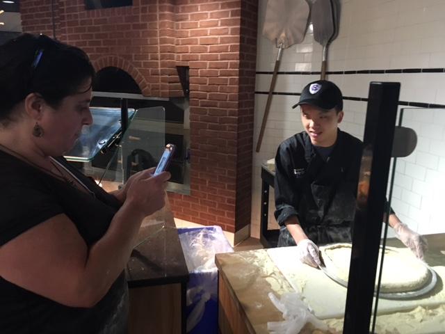 young man standing next to pizza making equipment while his co-worker looks on.